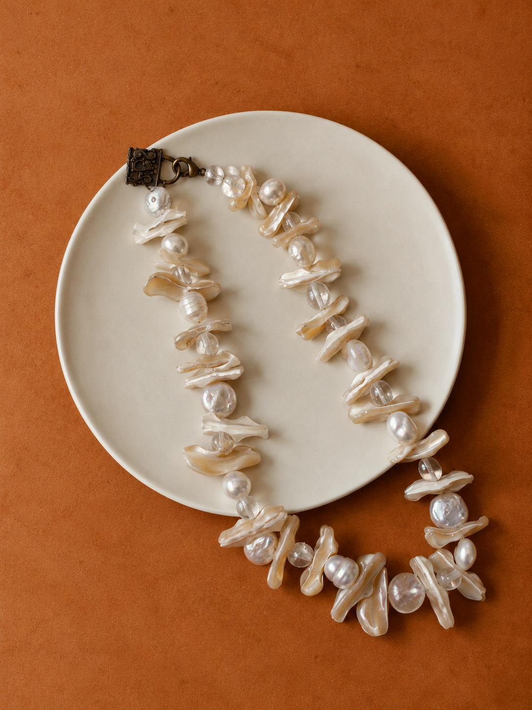 Pearl and shell necklace on a cream plate against an orange background