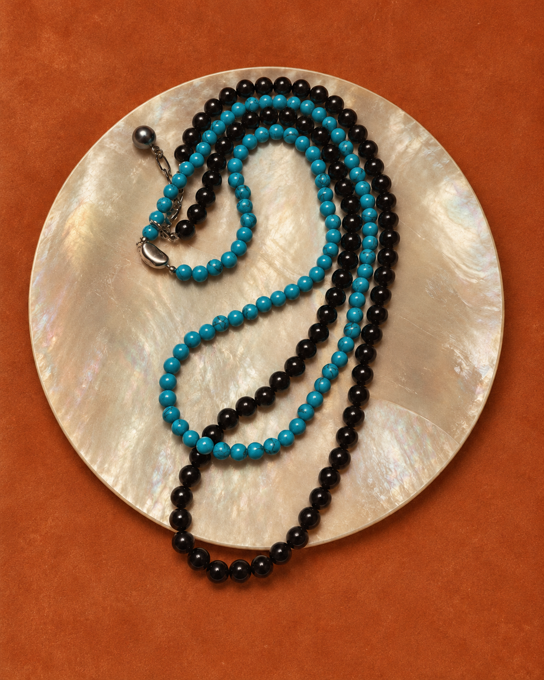 Turquoise bead necklace with a black bead necklace on a mother-of-pearl plate